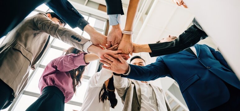 A down perspective reveals four diverse businesspeople standing in a circle stacking their hands. This image conveys the concepts of unity teamwork and global collaboration.