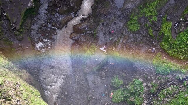 Rainbow arcs over muddy, mossy streambed at Tumpak Sewu