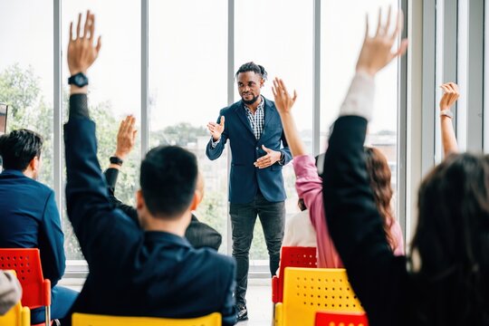 Business professionals come together for a corporate event featuring a conference and convention. Raised hands signify active participation in a meeting training seminar and discussions.