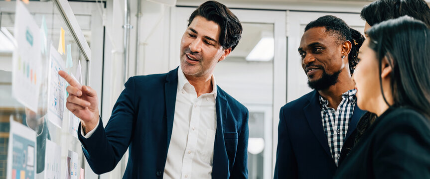Professionals collaborate in meeting, using glass board for brainstorming and strategy planning. Their teamwork, creative thinking, and leadership result in innovative solutions successful outcomes.