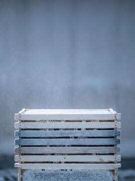 Frozen wooden beehive frames with honeycomb covered in winter frost and snow, cold atmosphere, apiculture concept, macro photography of beekeeping equipment in winter season, minimalist blue backgroun