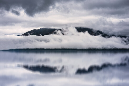 Alaska autumn cloudscape over a mountain summit with water reflection on Kenai River in Seward, USA