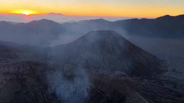 Sun rises over smoky volcanic Mount Bromo and Batok peak. Steam rises from crater edge