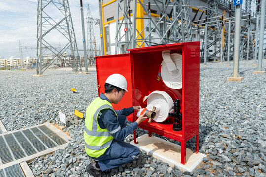 At a fire protection system inspection in an outdoor switchyard, a technician inspects a fire hose nozzle inside a red cabinet.
