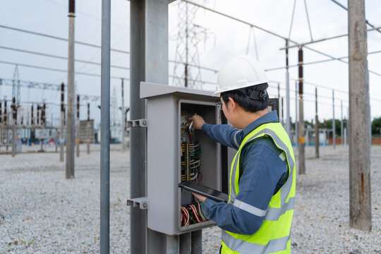 Cabinet inspection at a substation shows a technician using a tablet while checking wiring in an open control cabinet outdoors.