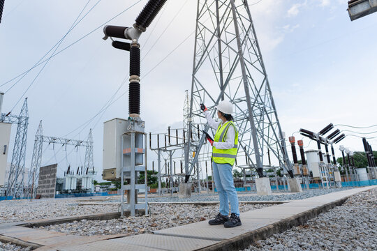 Outdoor switchyard pylon inspection shows the transmission tower and disconnect switch while a technician points at the tower with a tablet.