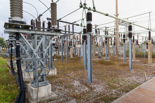 Showing high voltage equipment, the outdoor switchyard features a disconnect switch, insulators, busbars, and steel structures beside a lattice tower.