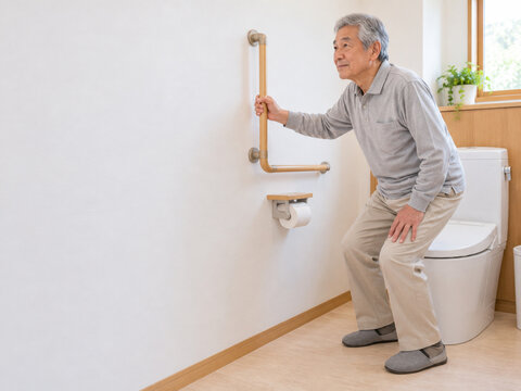 L字手すりにつかまってトイレの便座に座る高齢男性