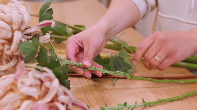 Bouquet making. Floristry workplace. Unrecognizable floral designer working with seasonal green leaves autumn flowers at wooden table.