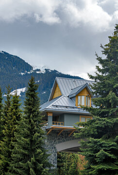 Gray suburban house with wooden arched entrance balcony and green trees against mountain background