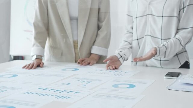 Two businesswomen examining financial data on charts and graphs during an office meeting, highlighting collaboration and strategy, close up. Business people concept