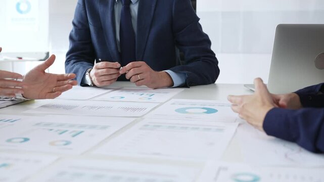 Business people team in formal suits reviewing printed charts and financial documents at office table, analyzing data for planning, growth, and corporate strategy development in office