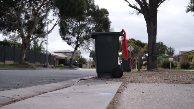 A wheelie bin with its lid flipped open after council waste collection on a suburban street curb in Melbourne, Victoria, Australia. Kerbside waste and municipal service in neighborhood
