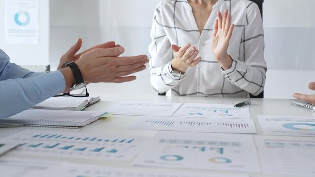 Business people team clapping hands in meeting celebrating success with financial charts, data analysis, and teamwork achievement in modern office