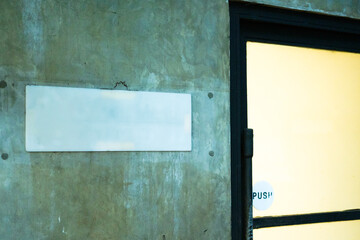 Blank white name board on wall beside a glass door with dim lighting, symbol of signage, notice, and communication, perfect for concepts of business, retail, and architectural environment. © Hermanthos