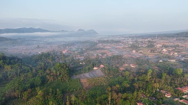 Sunrise aerial panorama of misty Teras Semeru rice terraces and village nestled in volcanic mountain valley.