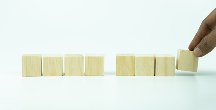 A hand placing eight wooden cube blocks arranged with four on the right and four on the left on white background, providing creative space for character or text placement, symbolizing balance,