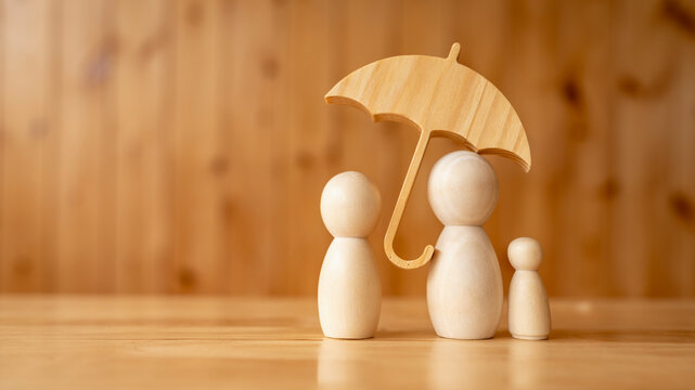 Family insurance and protection concept, wooden figures of parents and child standing under protective umbrella on table, symbolizing life coverage, healthcare support, and safety.