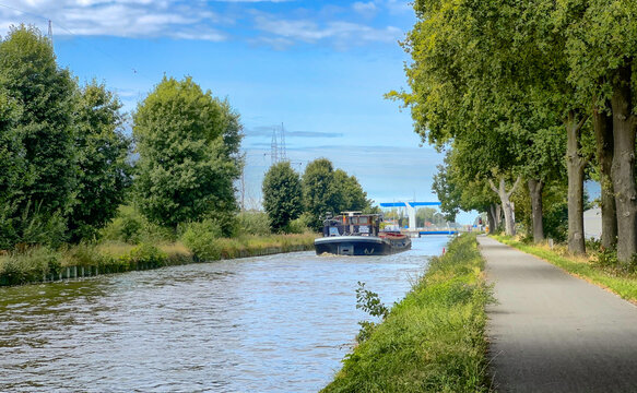 canal path lined with trees and calm water with small boat in distance, ideal for slow travel, cycling and riverside leisure,