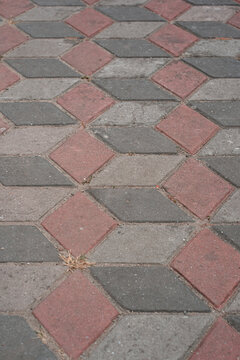 Perspective view of interlocking paving stones with red and grey colors creating a three-dimensional geometric cube pattern on the ground.