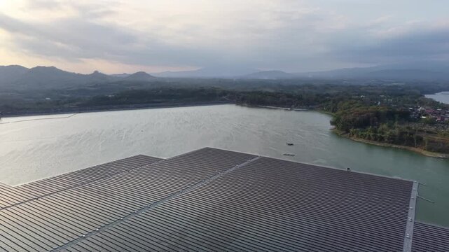 Drone aerial shot of expansive floating solar panels on reservoir with distant hills at dusk.
