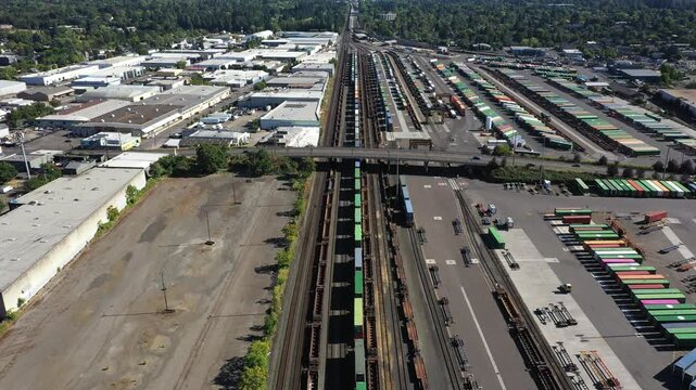 4K aerial drone footage of freight trains and rail yard in Portland, Oregon, USA, with railroad tracks, public transit bus facility, Holgate bridge and industrial transportation infrastructure