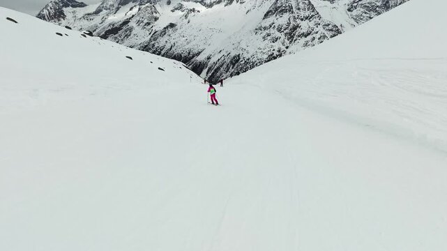 A skier in a bright pink suit carves down a wide groomed run at Arolla, Switzerland, rugged snow covered peaks closing the head of the valley ahead. POV hyperlapse shot