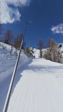 Riding a drag lift up a groomed run at Arolla, Switzerland, the tow bar in frame and larch trees and a pylon passing against a deep blue sky. POV shot