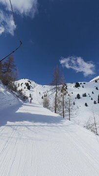 The view from a drag lift at Arolla, Switzerland, climbing a groomed run beside scattered larches as the slope opens onto a broad snow covered ridge. POV shot