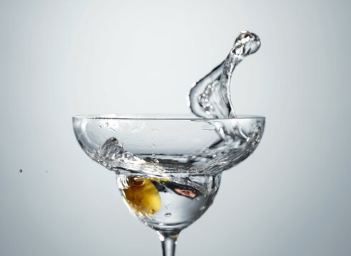 Clear martini glass with green olive in motion.