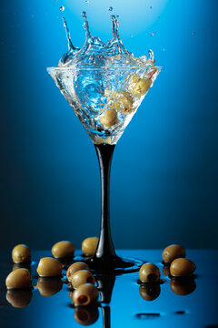 Martini with green olives on a wet table.