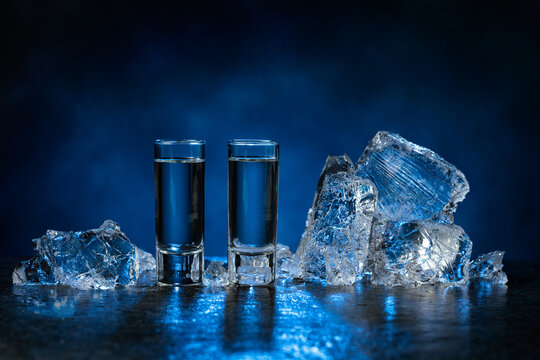 Shot glasses of vodka with ice shards on a dark blue background.