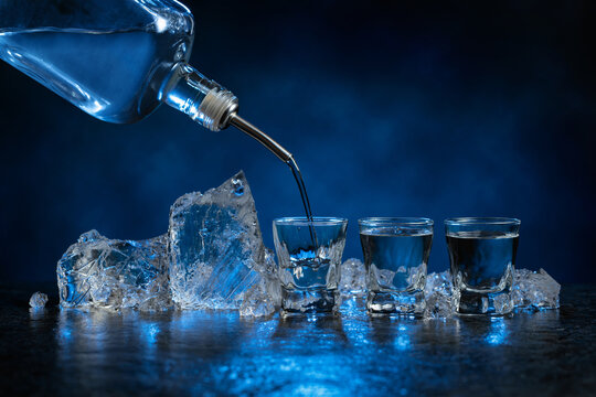 Shot glasses of vodka and ice on a dark blue background.