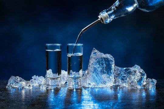 Shot glasses of vodka and ice on a dark blue background.