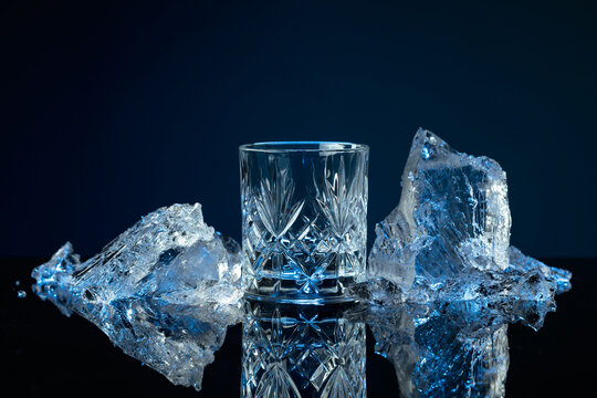 Crystal glass of vodka and ice shards against a black reflective background.