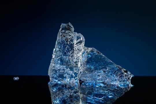 Broken ice with blue backlight on a black reflective background.