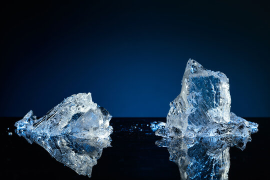 Broken ice on a black reflective background, with blue lighting.