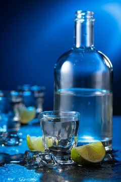 Vodka with lime slices on a black stone table.