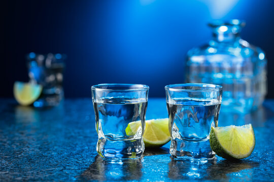 Vodka with lime slices on a black stone table.