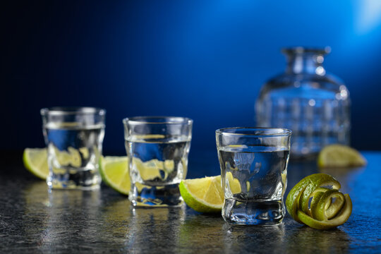 Vodka with lime slices on a black stone table.