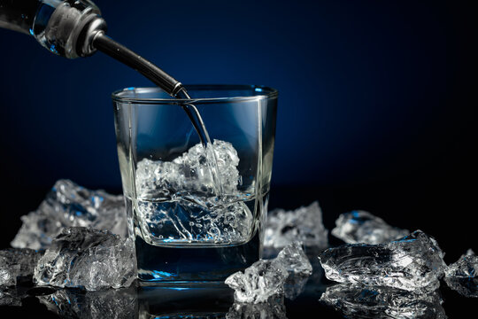 Crystal clear vodka or gin being poured over ice in a glass.