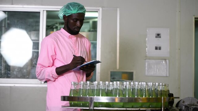 Worker of science in bottle beverage factory wearing safety hat working to packing and check drink machine conveyer belt before distribution to market business.