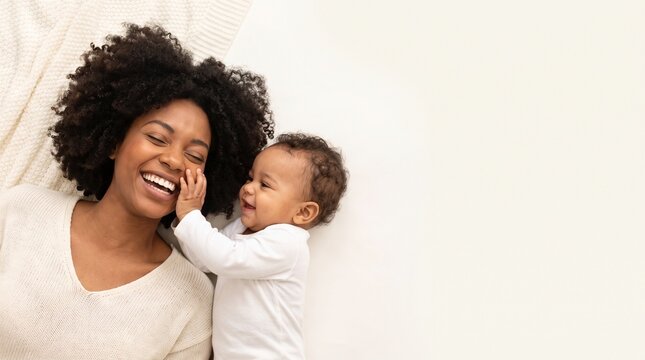 Joyful African American mother smiling with her adorable baby boy lying together at home