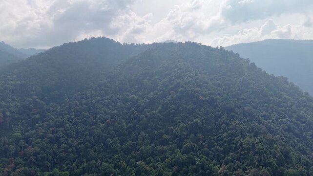 Aerial view captures dense forest covering mountains. Clouds drift above the lush trees at Lenggong