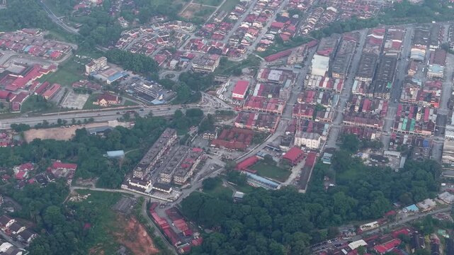 Aerial view reveals a town with red roofed buildings. Green parks separate neighborhoods and roads