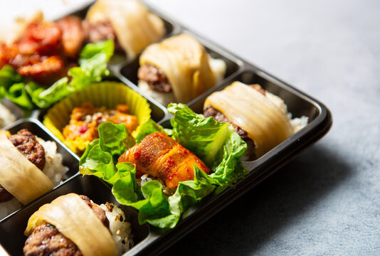 Gourmet Korean bento box featuring spicy stir-fried pork, beef bulgogi, and rice wrapped in kimchi and lettuce