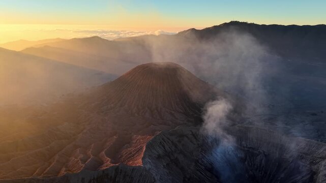 Golden light bathes a smoking volcano Mount Bromo. Mist curls from rugged crater edges