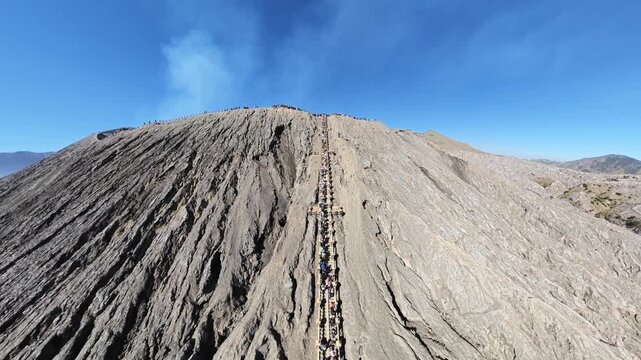 Drone fisheye panorama of Bromo crater staircase with hikers ascending volcanic ridge under clear blue sky.