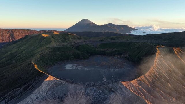 Sunrise bathes volcanic Mount Bromo caldera in warm light. Steam rises gently from its deep, dark basin