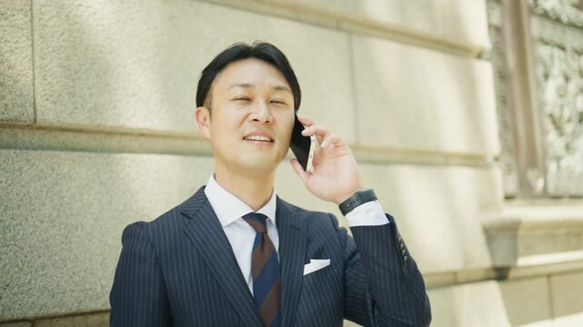 Businessman having a friendly phone conversation beside a stone wall